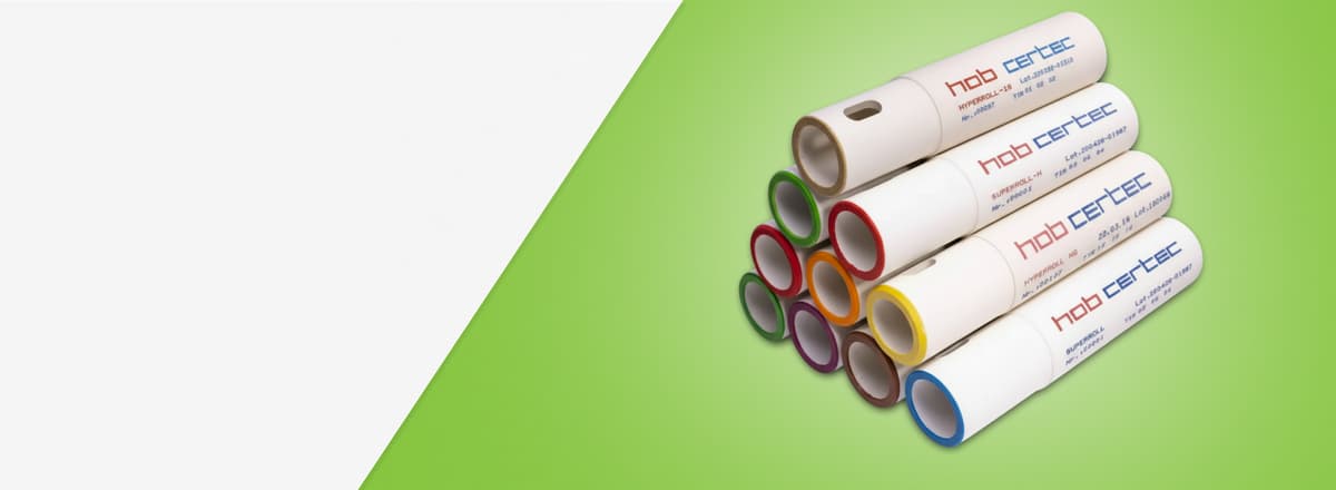 Uma pilha de rolos cerâmicos industriais brancos da marca Hob Certec, organizados em formato de pirâmide sobre um fundo verde.